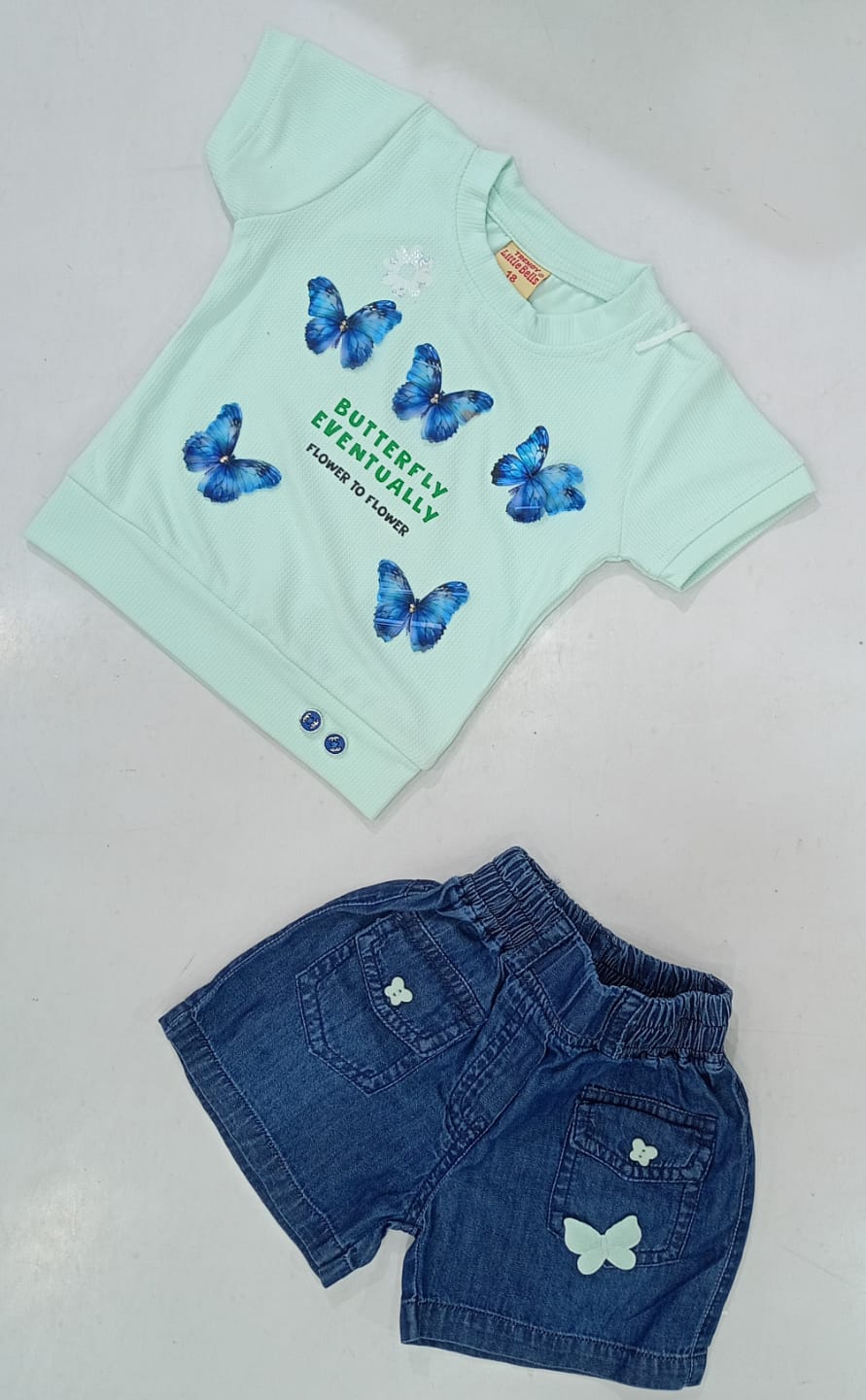 Mint green butterfly print tee laid flat with blue denim shorts featuring butterfly pocket detail