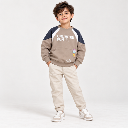 Boy wearing taupe Unlimited Fun sweatshirt with navy and white shoulder panels and cream joggers