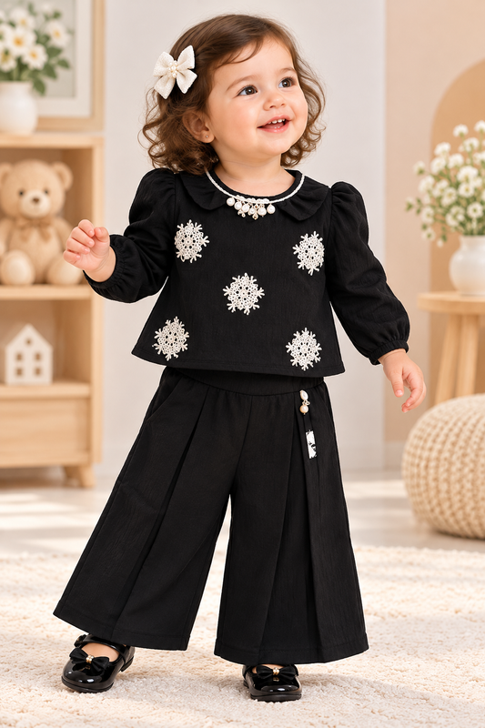 Baby girl wearing a black top with white floral embellishments and matching wide-leg palazzo pants