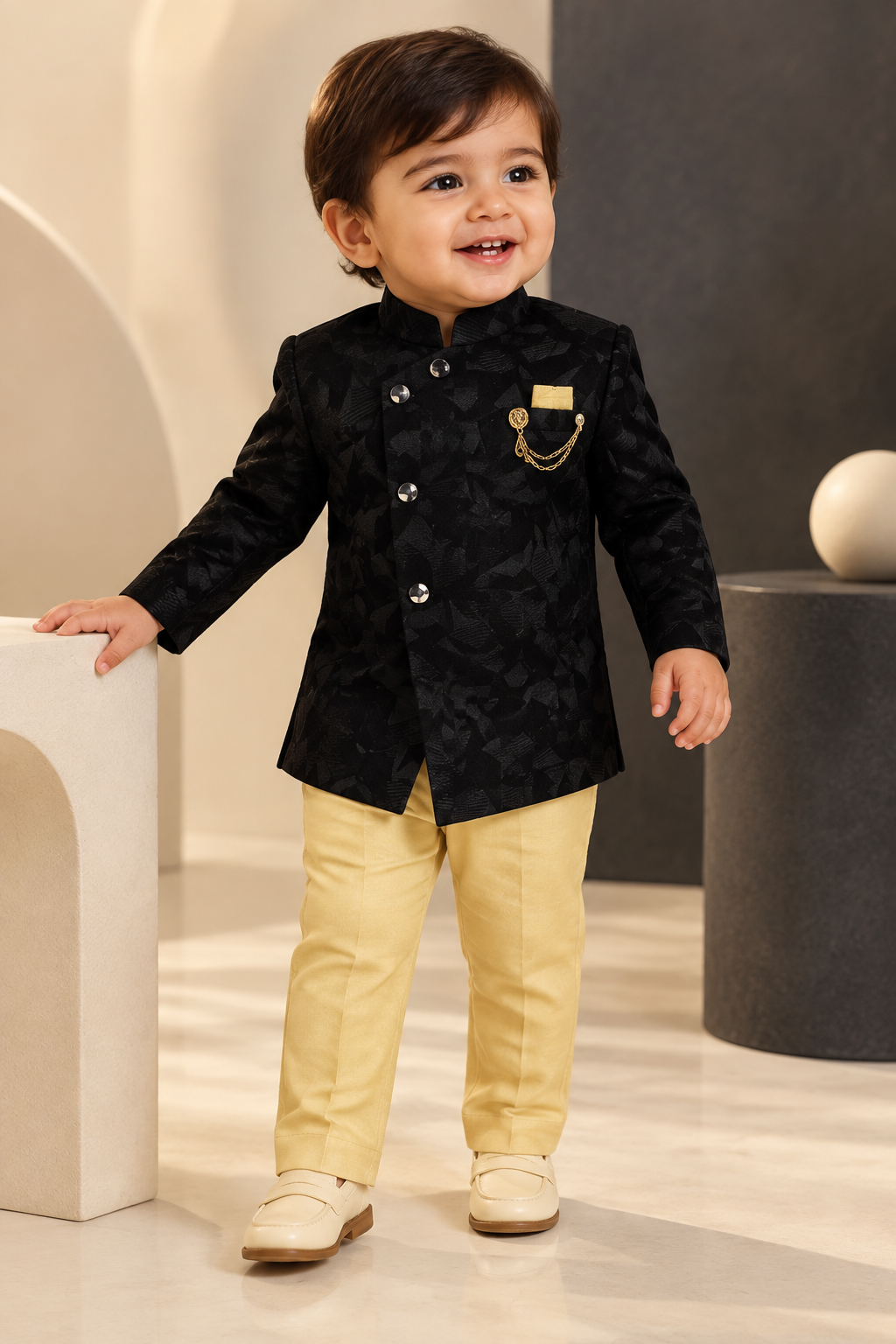 Toddler wearing black jacket with gold chain detail and beige pants